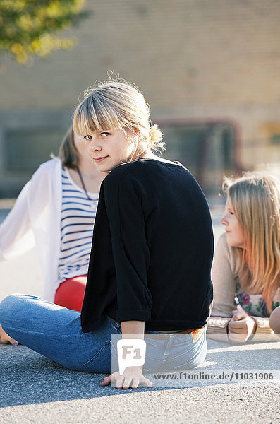 Blondes Teenager-Mädchen sitzt draußen mit zwei Freunden