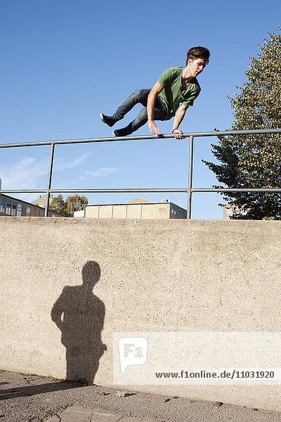 Teenage boy jumping over railings with shadow of another watching