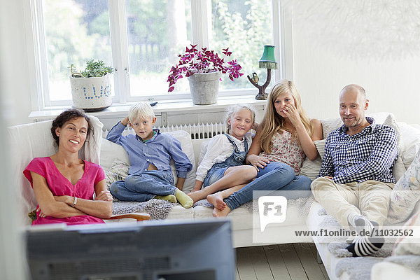 Family with three kids watching tv on sofa
