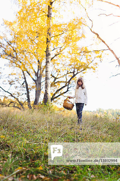 Mädchen geht mit Korb durch eine Herbstlandschaft
