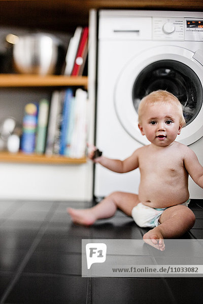 Baby boy wearing diaper sitting on kitchen floor