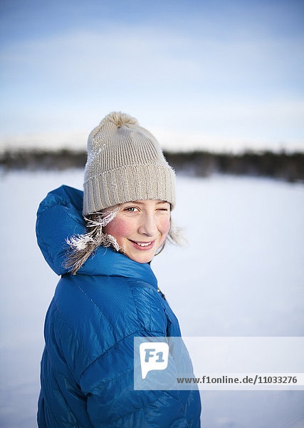 Mädchen mit Strickmütze zwinkert auf Schneefeld