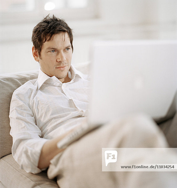 Ein Mann liegt auf einem Sofa mit einem Laptop auf dem Schoß.