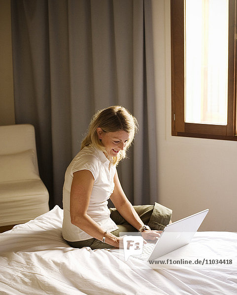 Scandinavian woman sitting on bed using a laptop.