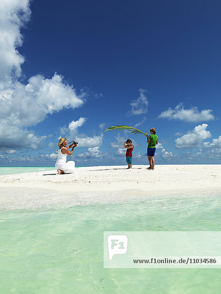 Jungen spielen am Sandstrand  während die Mutter ein Foto macht