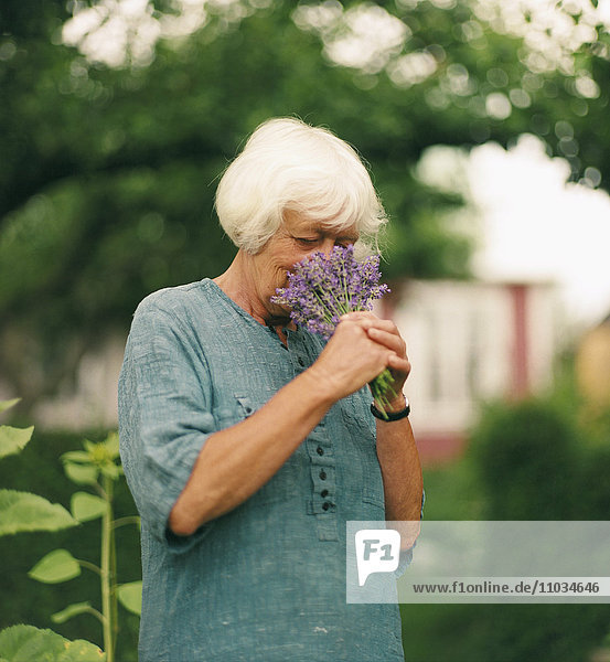 Ältere Frau riecht an Blumen