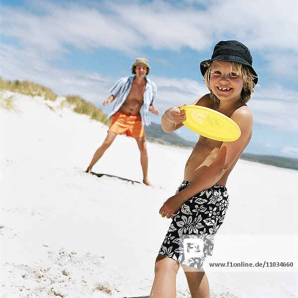 Vater und Sohn spielen mit einer Flugscheibe am Strand  Schweden.
