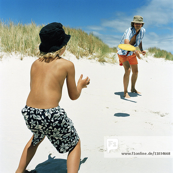 Father and son playing with flying disc on beach  Sweden.