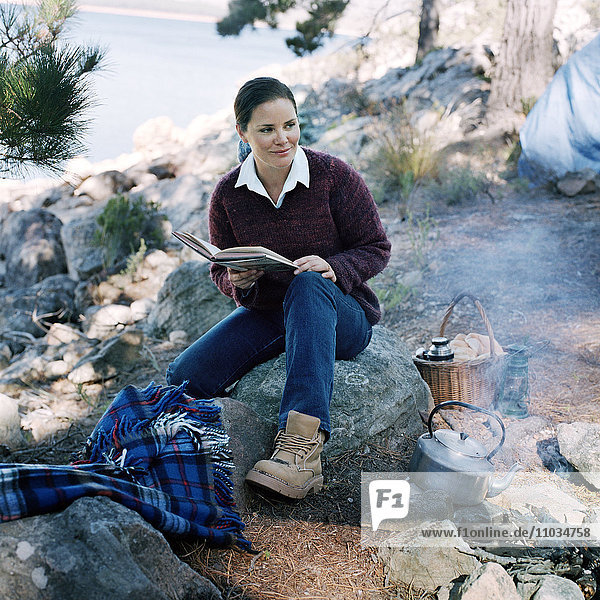 Porträt einer Frau  die an einem Lagerfeuer sitzt und ein Buch liest  Schweden.
