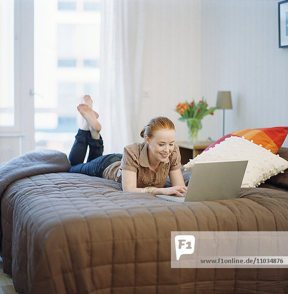 Frau auf einem Bett liegend mit einem Laptop.