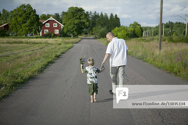 Father walking with son on road  boy holding flowers