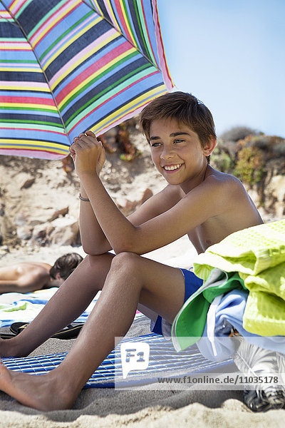 Lächelnder Junge am Strand sitzend
