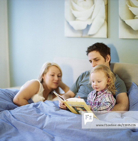 A mother and father reading for their daughter.