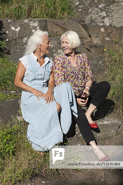 Two mature friends sitting on stone