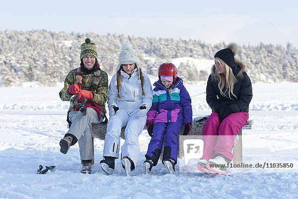 Mother with tree daughters sitting on bench and putting on ice-skates