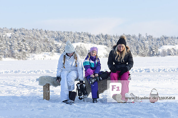 Three sisters sitting on bench and putting on ice-skates