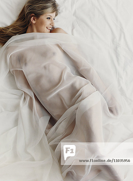 Eine nackte Frau in einem Bett mit einem durchsichtigen Laken.