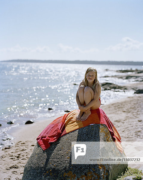 Mädchen sitzt auf einem großen Felsen am Strand  Schweden.