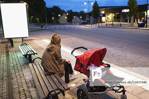Frau  die auf einer Bank mit einem Kinderwagen wartet  Schweden.