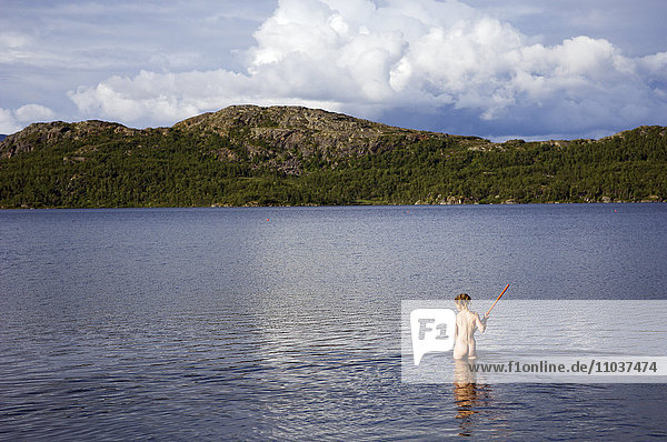 Junges nacktes Mädchen harkt auf dem Grund eines Sees  Schweden.