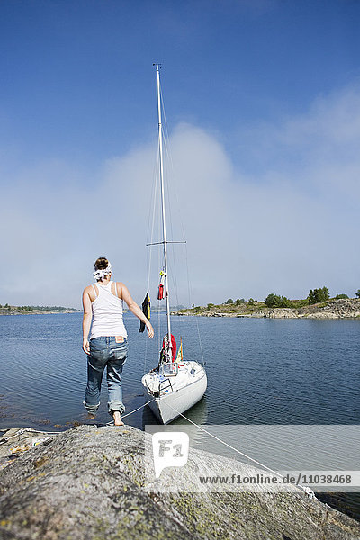 Frau auf einem Felsen neben einem Segelboot  Schweden.