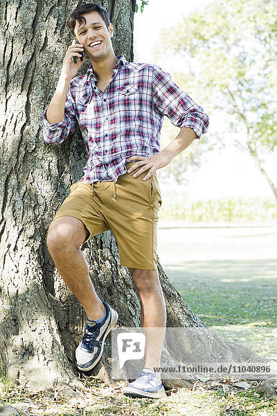 Man leaning against tree using cell phone