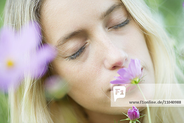 Junge Frau riecht Blumen mit geschlossenen Augen  Porträt