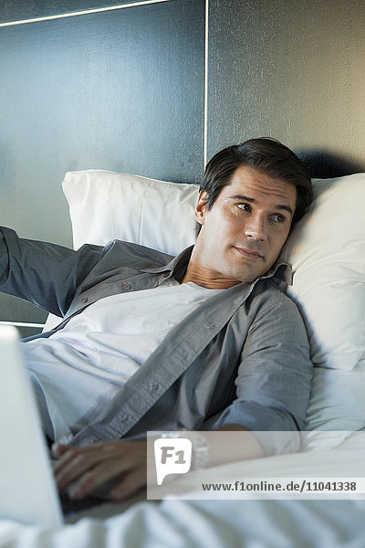 Man relaxing in bed with laptop computer