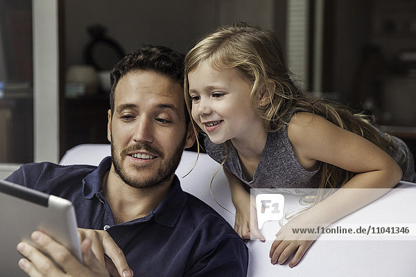 Man showing daughter video streaming on digital tablet