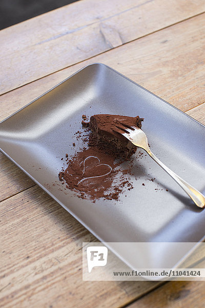 Herz aus Kakaopulver und halb gegessenem Schokoladenkuchen