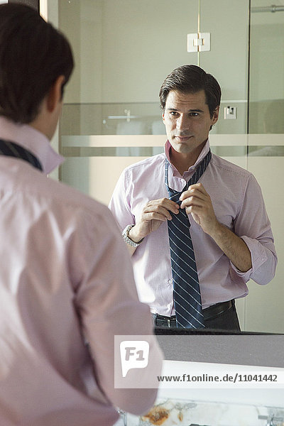 Man adjusting necktie in bathroom mirror
