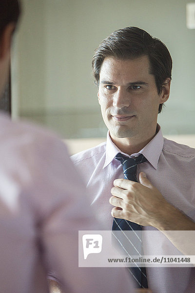 Man adjusting his tie in mirror