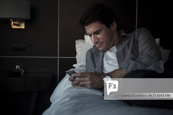 Mann entspannt auf dem Bett mit Multimedia-Smartphone