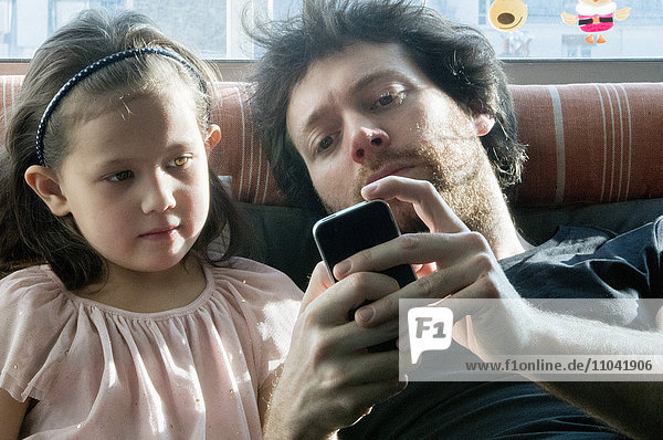 Father and young daughter looking at smartphone together