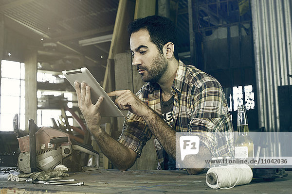 Mann in der Werkstatt mit digitalem Tablett für den Zugriff auf Reparaturanleitungen im Internet