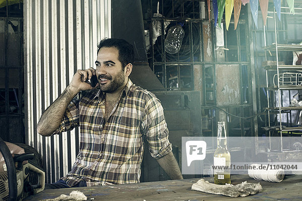 Mann beim Bier trinken und telefonieren in der Werkstatt