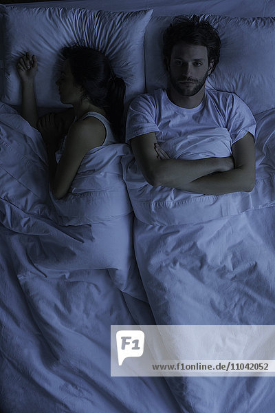 Wach liegender Mann im Bett neben schlafender Frau