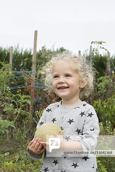 Kleines Mädchen mit Melone im Garten