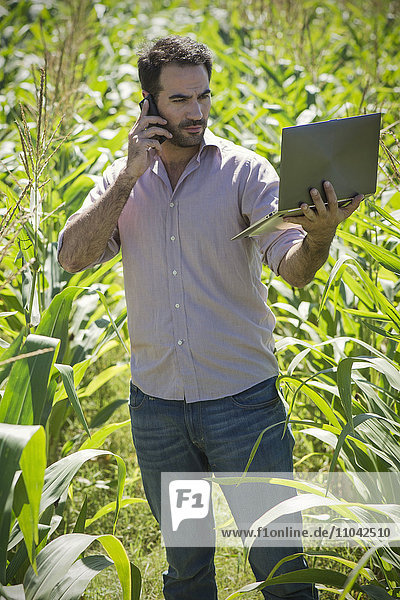 Mann  der einen Laptop benutzt  während er im Kornfeld steht.