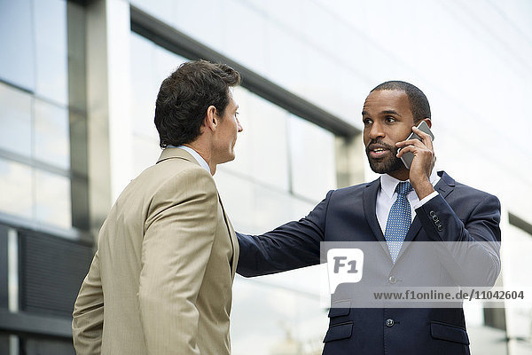 Businessman standing with colleague outdoors  talking on cell phone