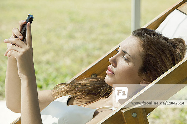 Junge Frau beim Sonnenbaden auf das Smartphone schauen