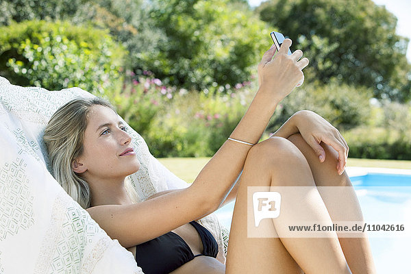 Frau entspannt am Pool  mit dem Smartphone ein Selfie zu nehmen