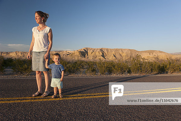 Mutter und Kleinkind gehen gemeinsam auf gepflasterter Straße durch die Wüste