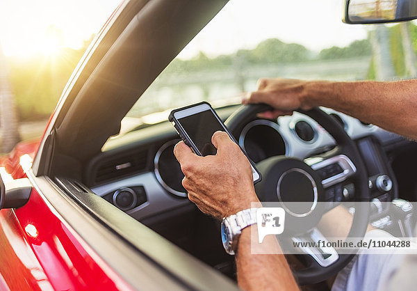 Caucasian man using cell phone and driving convertible