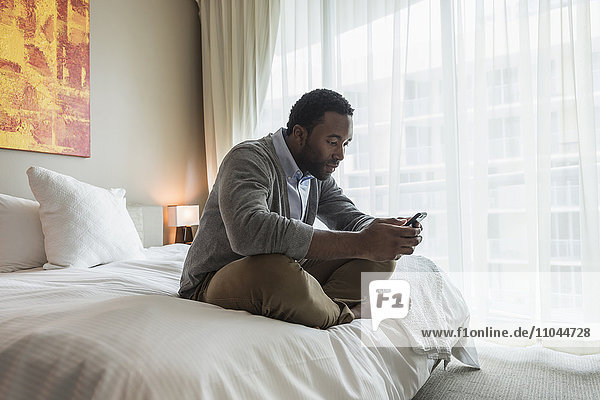 Schwarzer Mann benutzt Mobiltelefon auf dem Bett