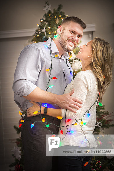 Caucasian couple wrapped in Christmas lights