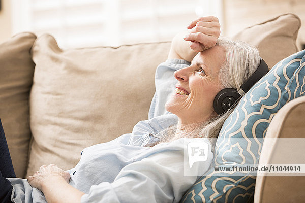 Kaukasische Frau hört auf dem Sofa Kopfhörer