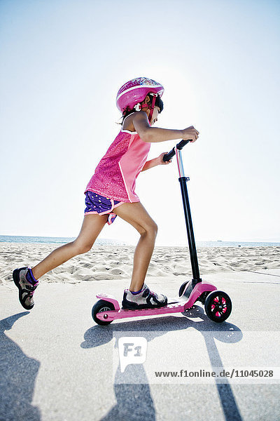 Mixed race girl riding scooter at beach