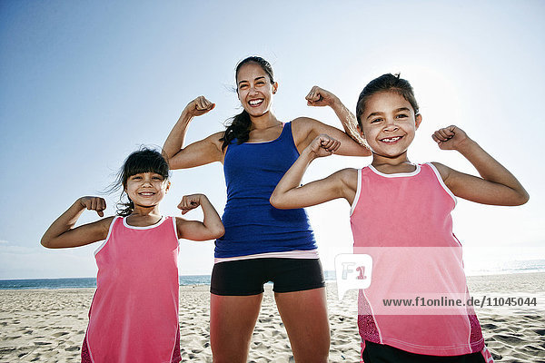 Mother and daughters flexing muscles at beach
