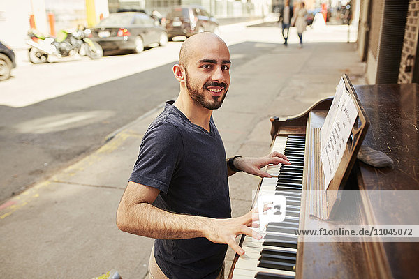 Hispanic man playing piano on city sidewalk